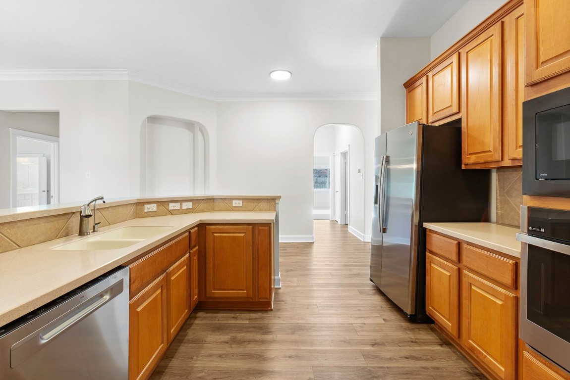 10805 Ariock Lane Austin, TX 78739 - Photo 12 of 40 Kitchen with appliances with stainless steel finishes, tasteful backsplash, brown cabinetry, ornamental molding, and arched walkways