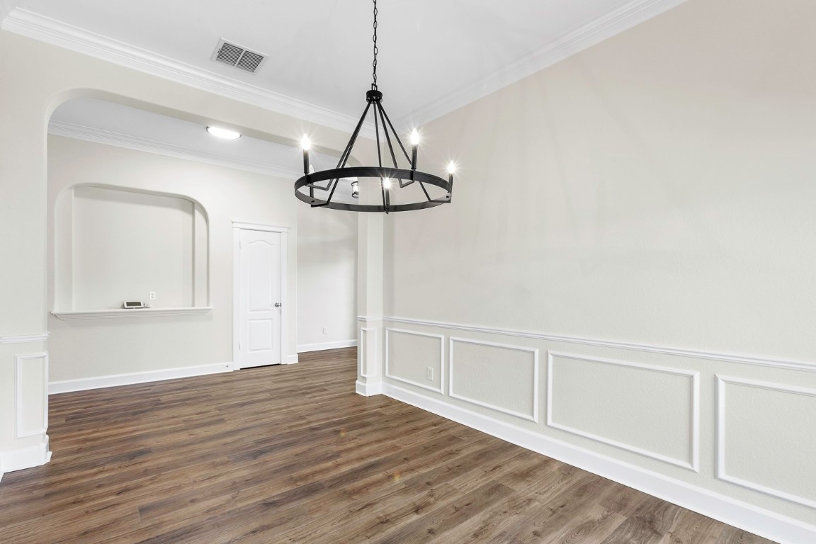 10805 Ariock Lane Austin, TX 78739 - Photo 21 of 40 Unfurnished dining area with a decorative wall, dark wood-style floors, crown molding, wainscoting, and a chandelier