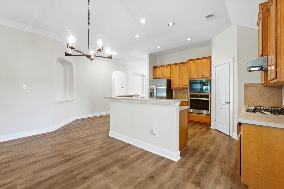 10805 Ariock Lane Austin, TX 78739 - Photo 10 of 40 Kitchen with arched walkways, pendant lighting, a kitchen island with sink, brown cabinets, and a chandelier