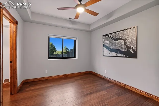 an empty room with wooden floor chandelier fan and windows