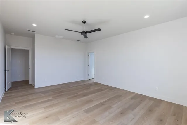 an empty room with wooden floor fan and windows