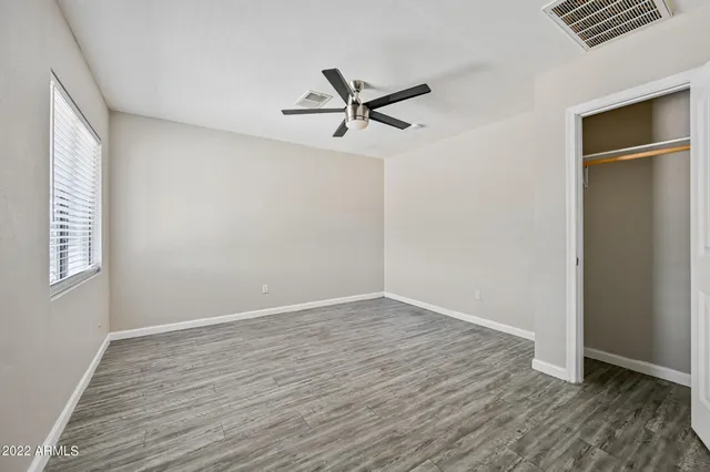 an empty room with wooden floor a ceiling fan and windows