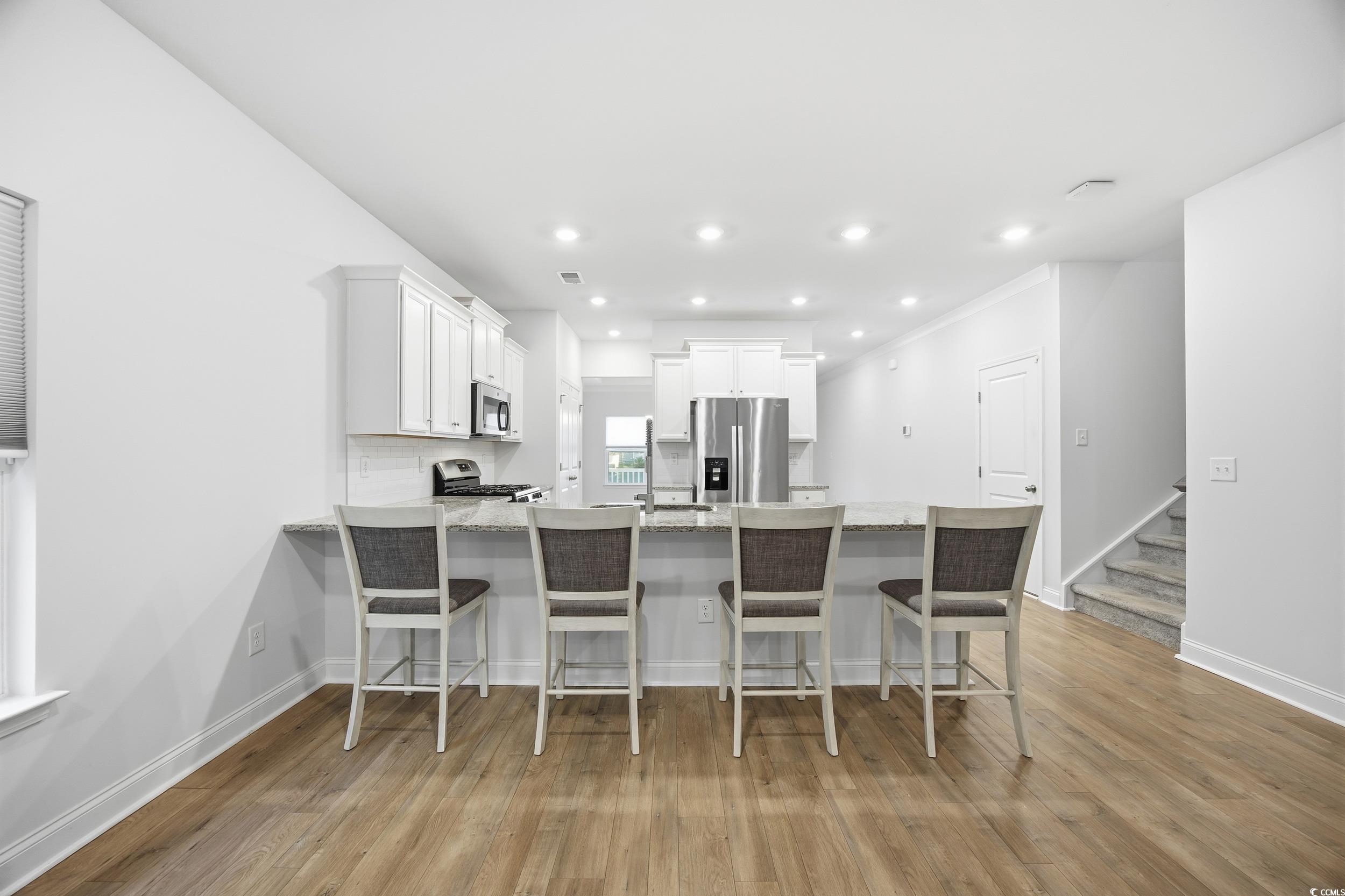 386 Harbison Circle Myrtle Beach, SC 29579 - Photo 11 of 34 Kitchen with a peninsula, a breakfast bar, appliances with stainless steel finishes, white cabinetry, and light wood-type flooring