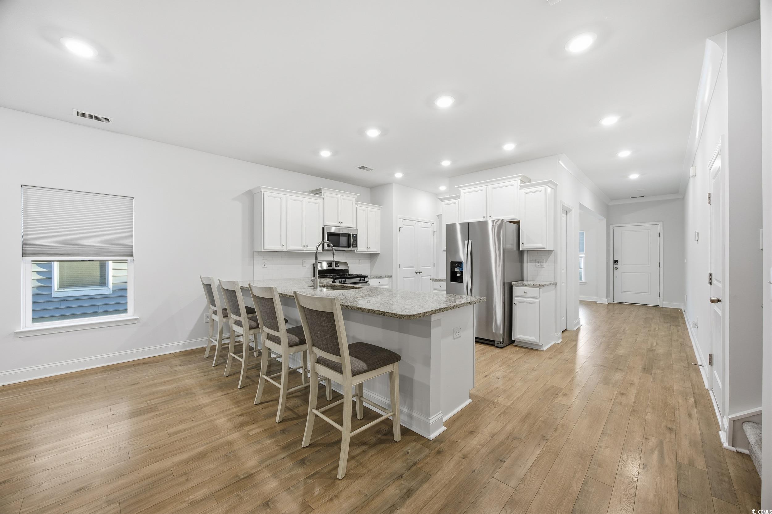 386 Harbison Circle Myrtle Beach, SC 29579 - Photo 10 of 34 Kitchen featuring appliances with stainless steel finishes, white cabinets, a peninsula, a kitchen bar, and light stone countertops