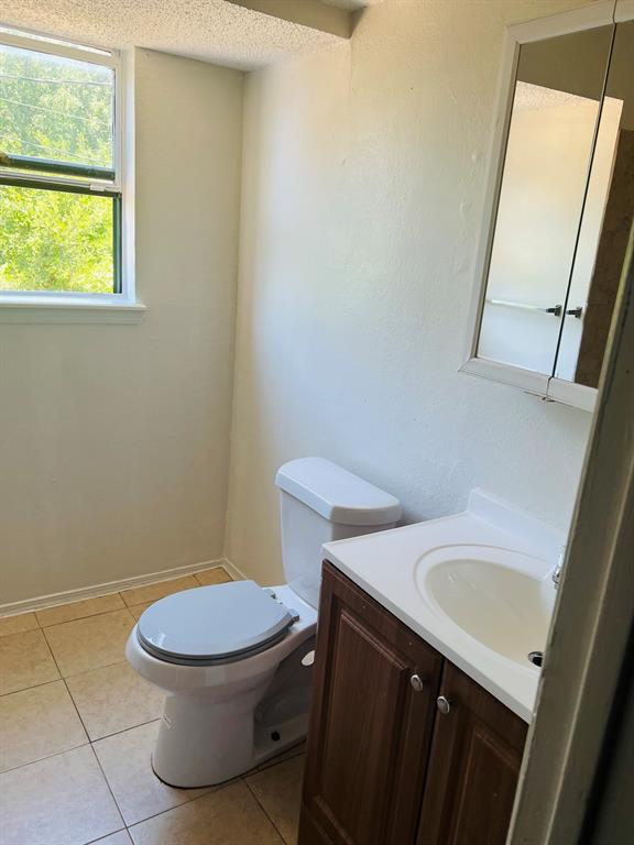 6320 Midway Road, Unit C Springtown, TX 76082 - Photo 10 of 11 Bathroom featuring a single-pane window, ceramic tile flooring, a wood-finish vanity with an integrated sink, a white toilet, and a mirrored medicine cabinet