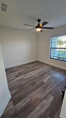 an empty room with wooden floor fan and windows