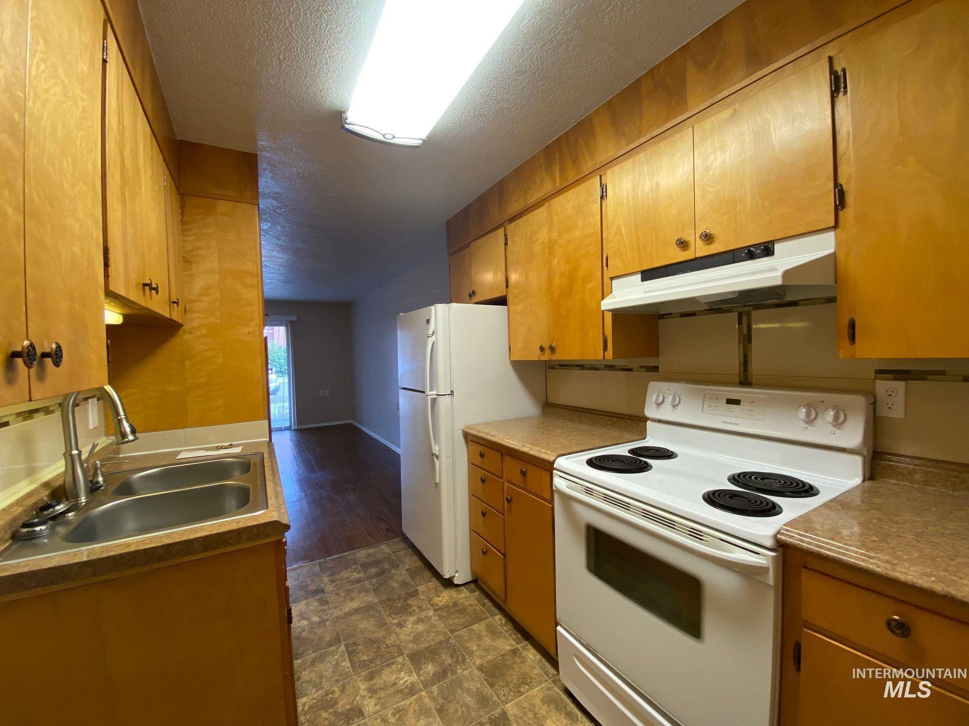 160 Northwest 3rd Street Ontario, OR 97914 - Photo 2 of 4 Kitchen featuring white appliances, under cabinet range hood, a textured ceiling, brown cabinets, and stone finish flooring