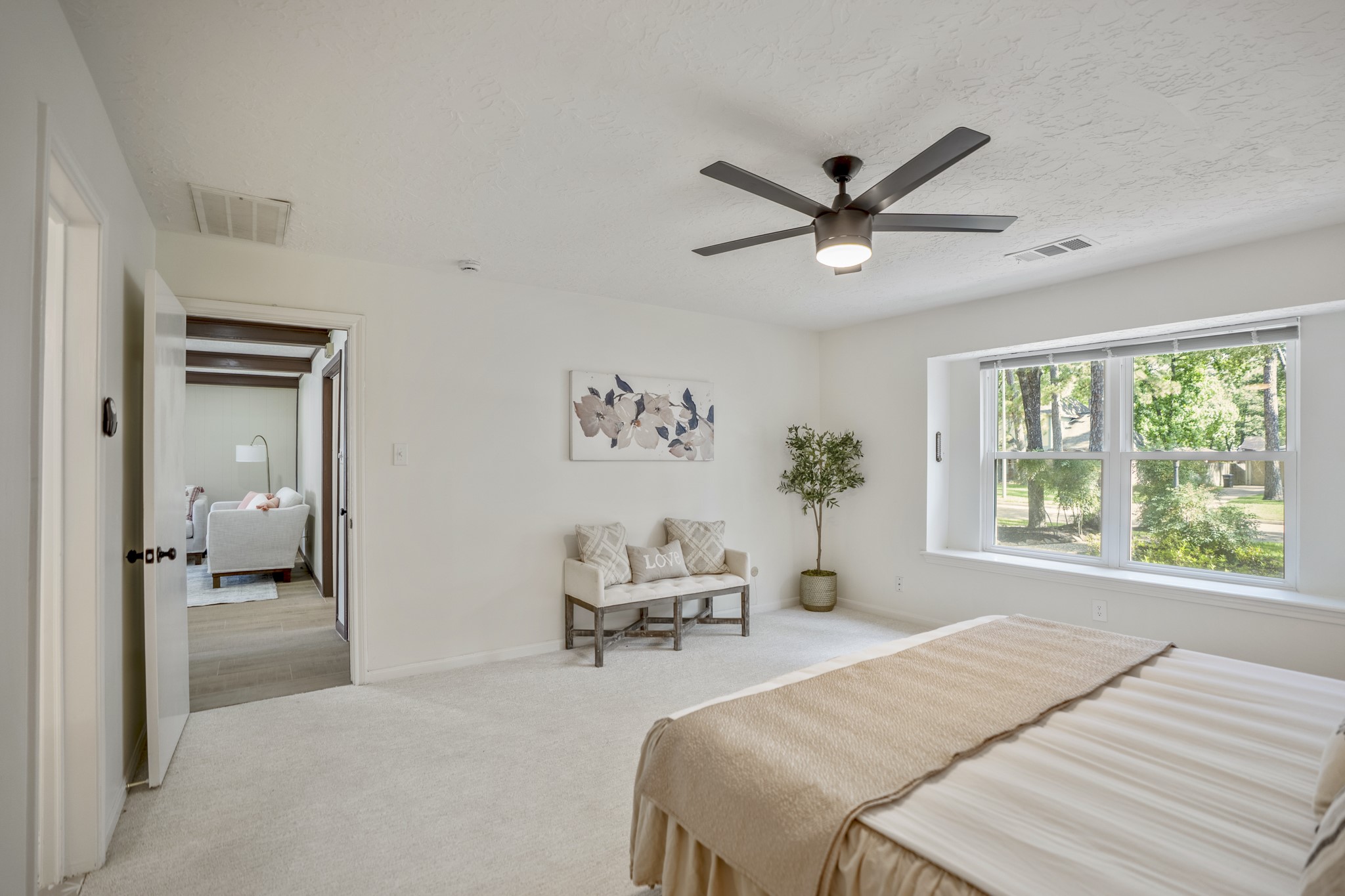 6303 Larkmount Drive Spring, TX 77389 - Photo 26 of 50 Stepping back out from the ensuite, the primary bedroom feels bright and peaceful with the large window bringing in natural light and greenery from outside. The bathroom is now behind us, while the doorway ahead gives a glimpse back into the family room, keeping the suite connected while still feeling nicely tucked away.