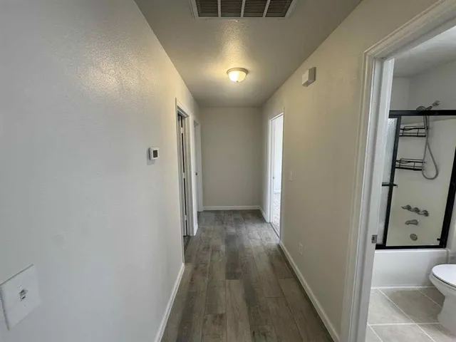 a view of a hallway with wooden floor and a bathroom
