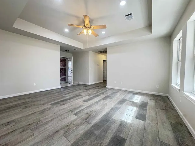 an empty room with wooden floor chandelier fan and windows