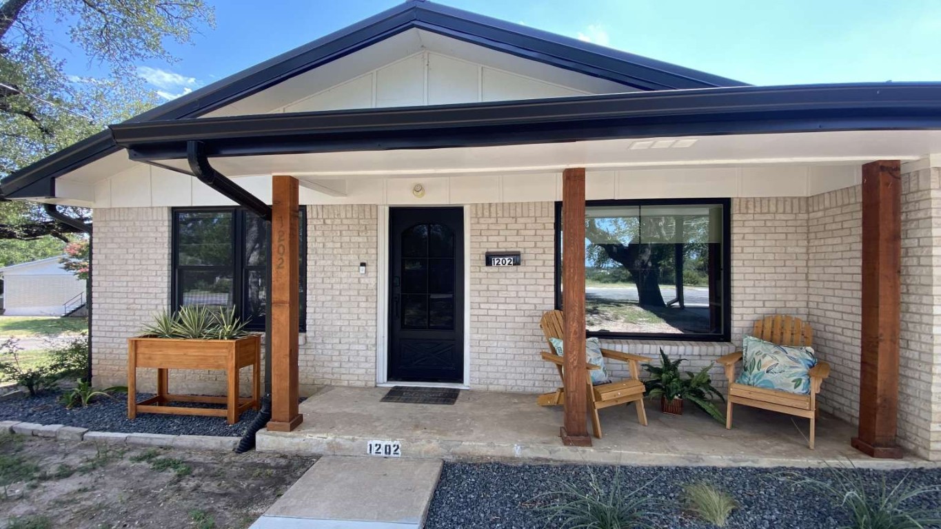 Doorway to property with covered porch, brick siding, and board and batten siding