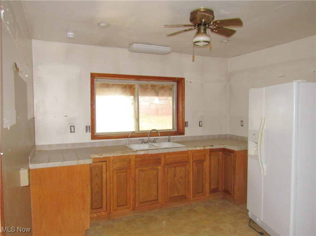 2218 Lake Road Akron, OH 44312 - Photo 9 of 20 Kitchen featuring white refrigerator with ice dispenser, brown cabinets, tile countertops, light floors, and a sink