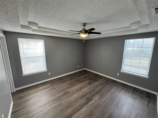 an empty room with wooden floor chandelier fan and windows