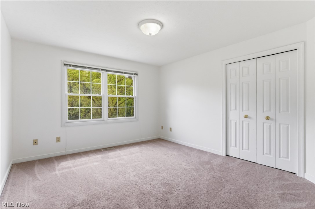 11678 Dunham Road Northfield, OH 44067 - Photo 27 of 38 Bright interior room featuring a double window, wall-to-wall carpeting, white walls, and a bi-fold closet with brass hardware