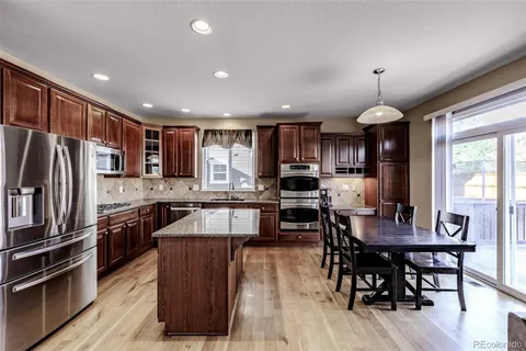 a kitchen with stainless steel appliances granite countertop a stove top oven a sink dishwasher a dining table and chairs with wooden floor