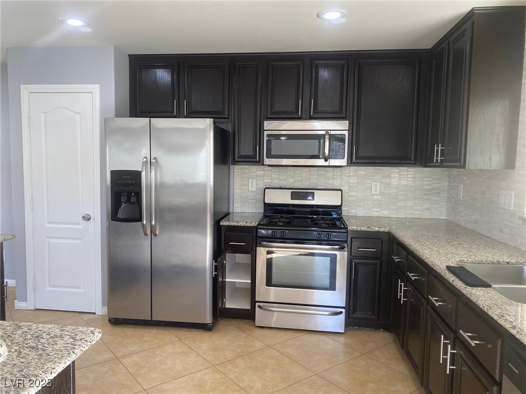 9541 Vast Valley Avenue Las Vegas, NV 89148 - Photo 10 of 32 Kitchen featuring stainless steel appliances, light stone counters, dark cabinetry, light tile patterned floors, and recessed lighting