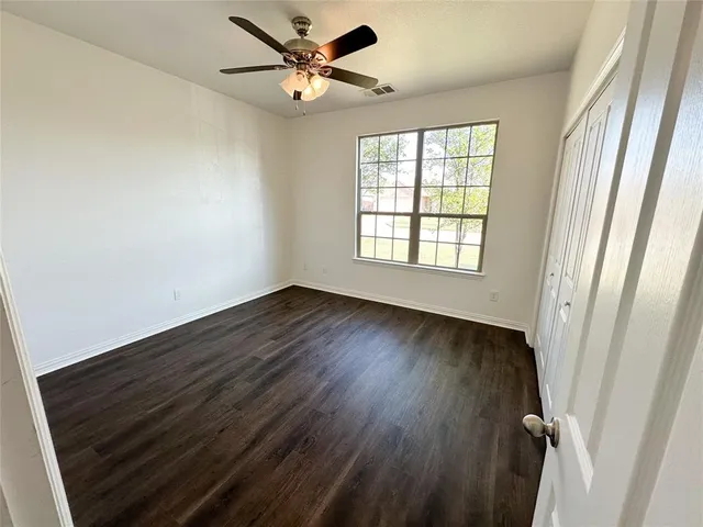 an empty room with wooden floor fan and windows