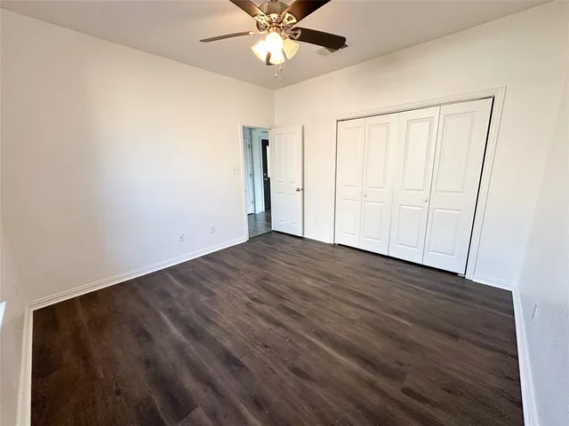 an empty room with wooden floor fan and windows