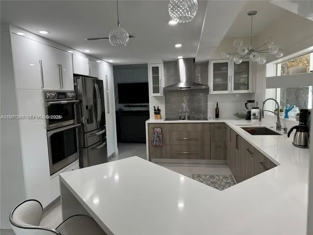a kitchen with stainless steel appliances a sink a stove a refrigerator cabinets and chairs