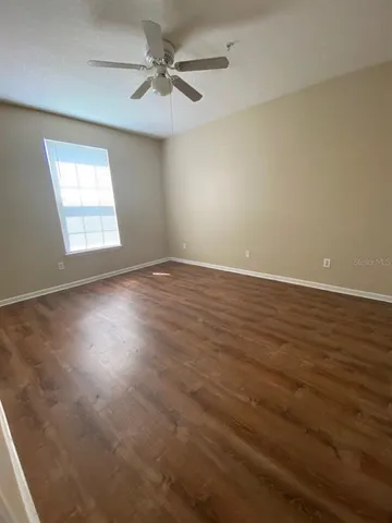 an empty room with wooden floor fan and windows
