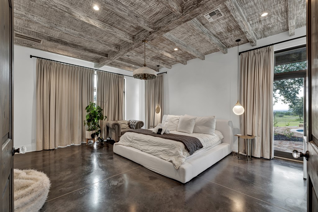 2975 Bear Creek Road Fredericksburg, TX 78624 - Photo 7 of 53 a spacious bedroom with a bed a chandelier and a large window with outer view