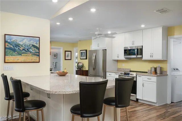 a kitchen with stainless steel appliances kitchen island granite countertop a stove top oven a sink dishwasher a refrigerator and cabinets with wooden floor