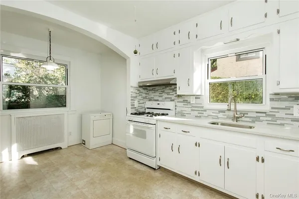 a kitchen with granite countertop white cabinets white appliances a sink and a window