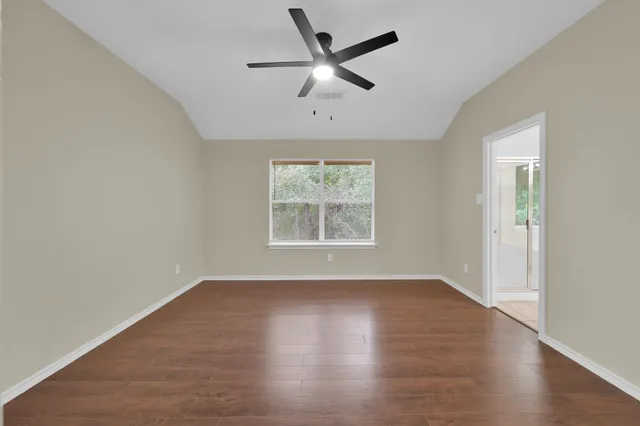 an empty room with wooden floor ceiling fan and windows