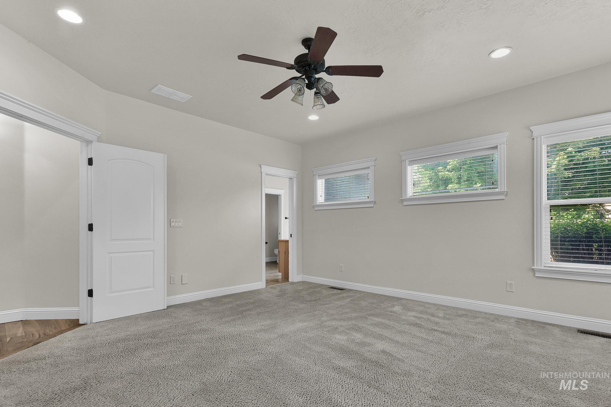 2172 West Cedar Grove Street Meridian, ID 83646 - Photo 14 of 49 Spacious room featuring light gray carpeting, multiple windows with white trim, and a ceiling fan with integrated lighting