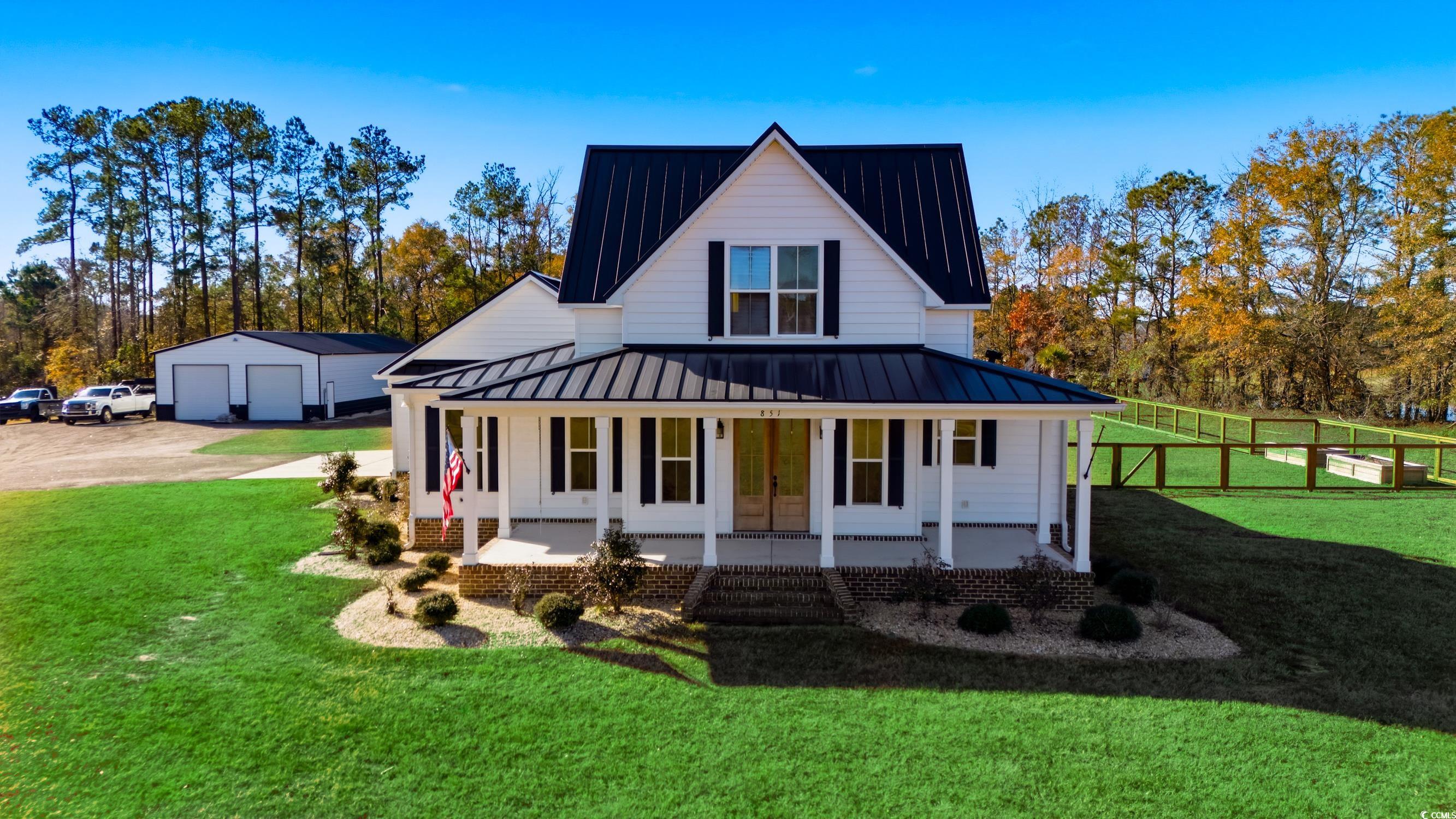 Modern farmhouse featuring a front lawn, a metal roof, a porch, a standing seam roof, and a detached garage