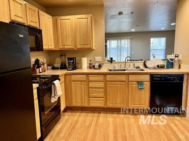 6498 South Lighthouse Place Boise, ID 83709 - Photo 3 of 16 Kitchen featuring black appliances, light countertops, light wood finish cabinets, light wood-style flooring, and a textured ceiling