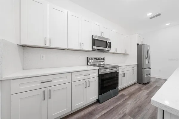 a kitchen with stainless steel appliances granite countertop white cabinets a sink a stove a refrigerator and microwave with wooden floor