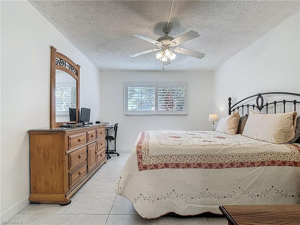 175 Turtle Lake Court, Unit 108 Naples, FL 34105 - Photo 11 of 17 Bedroom with light tile patterned floors, baseboards, a textured ceiling, a ceiling fan, and a desk