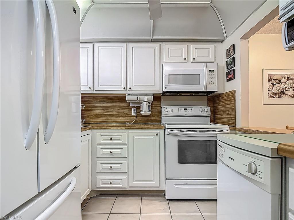 175 Turtle Lake Court, Unit 108 Naples, FL 34105 - Photo 3 of 17 Kitchen featuring white appliances, light tile patterned floors, white cabinets, and dark countertops