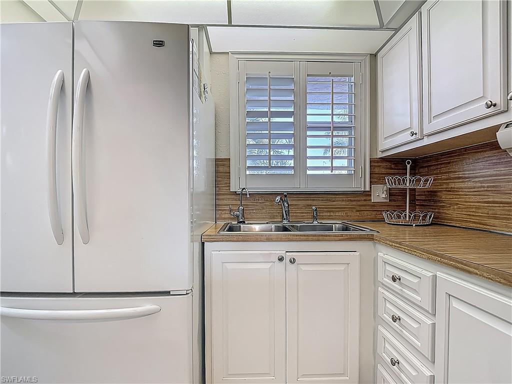 175 Turtle Lake Court, Unit 108 Naples, FL 34105 - Photo 4 of 17 Kitchen with freestanding refrigerator, a sink, white cabinets, and decorative backsplash