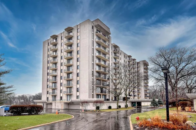 a front view of a building with lot of cars and trees