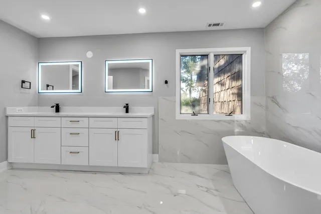a spacious bathroom with double vanity a mirror a bathtub and a window