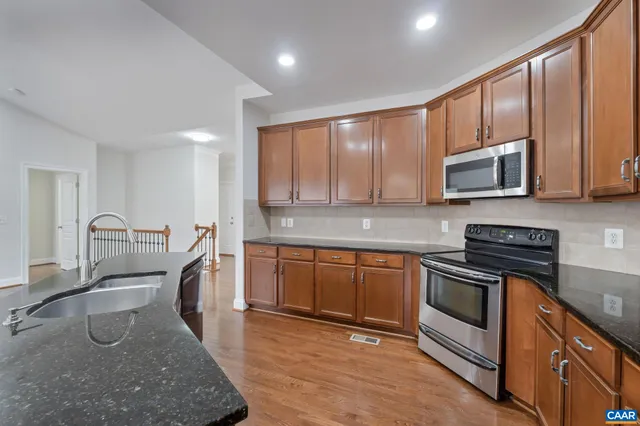 a kitchen with stainless steel appliances granite countertop a refrigerator a stove a sink dishwasher and a oven with wooden floor