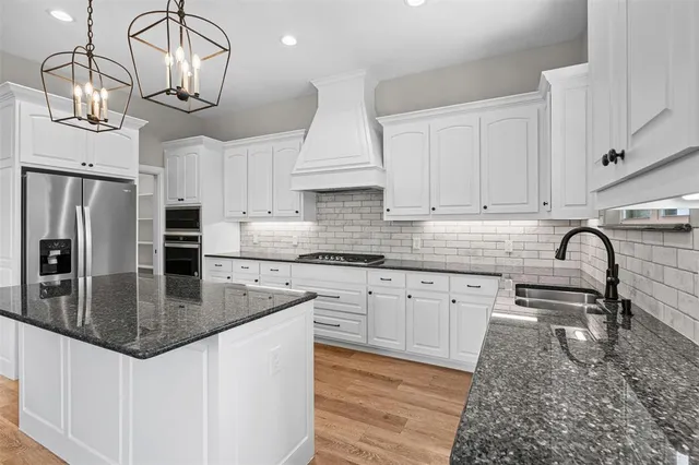 a large kitchen with stainless steel appliances granite countertop a stove a sink dishwasher a refrigerator and white cabinets with wooden floor