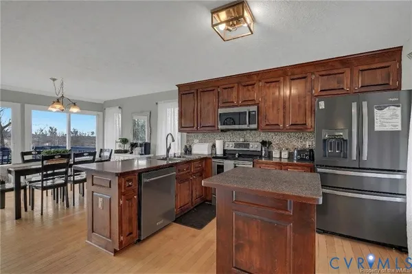 a kitchen with stainless steel appliances granite countertop a stove top oven a sink dishwasher a dining table and chairs with wooden floor