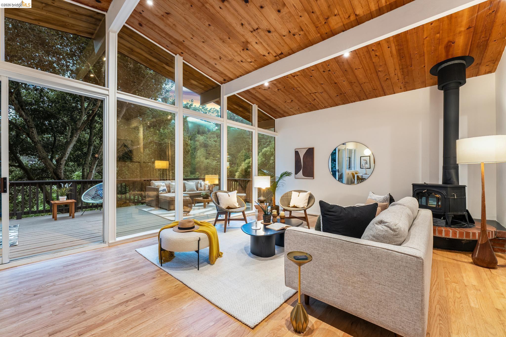 6645 Heather Ridge Way Oakland, CA 94611 - Photo 16 of 61 Living area with wood-finish flooring, a wood-paneled vaulted ceiling, and a wood-burning stove on a brick hearth
