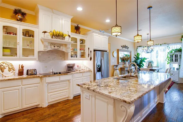 a kitchen with granite countertop a stove a sink a refrigerator and white cabinets with wooden floor