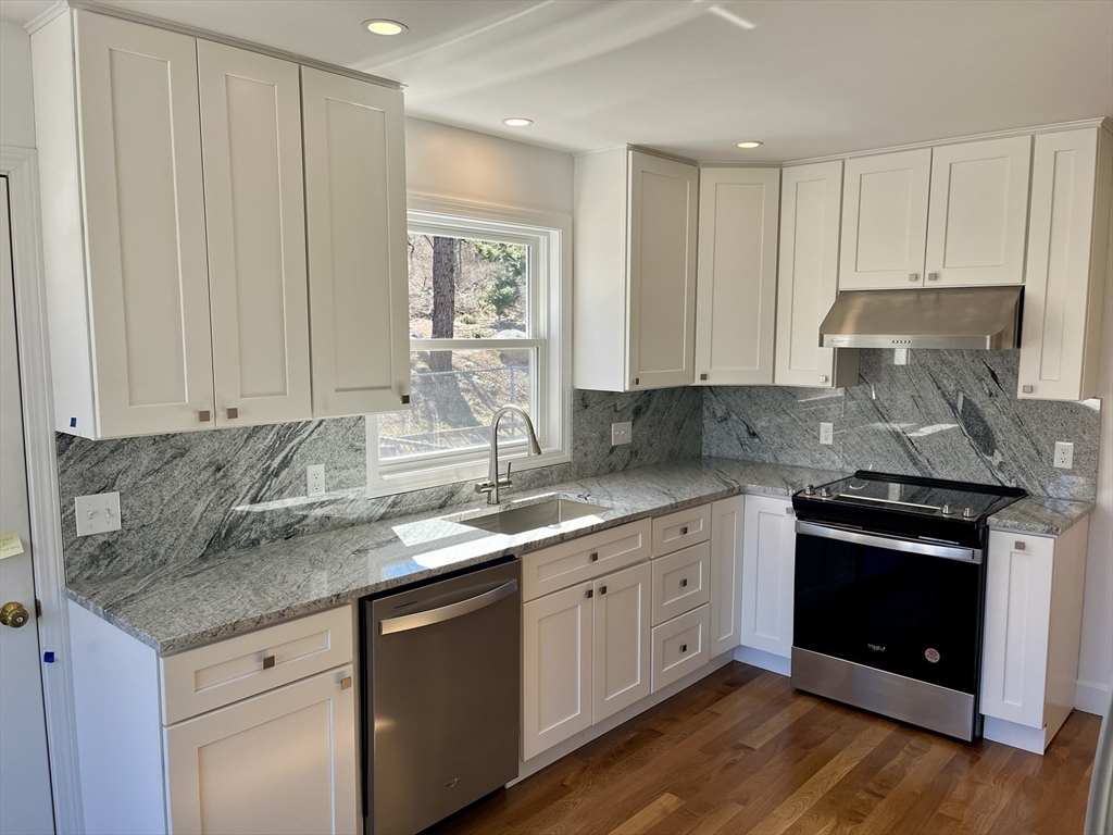 a kitchen with granite countertop stainless steel appliances white cabinets granite counter tops and a wooden floors