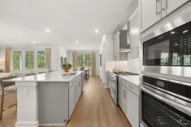 a kitchen with stainless steel appliances kitchen island granite countertop a stove a sink dishwasher and white cabinets with wooden floor