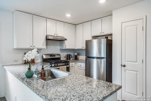 a kitchen with stainless steel appliances granite countertop a refrigerator a stove a sink a refrigerator and white cabinets