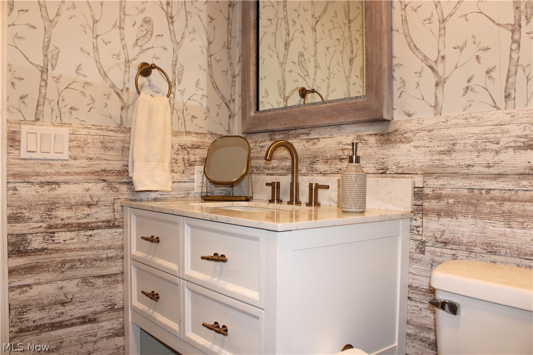 5547 River Styx Road Medina, OH 44256 - Photo 33 of 45 Bathroom featuring a white vanity with bronze hardware, a light-toned countertop, a bronze-finish faucet, a wood-framed mirror, and wood-panel wainscoting