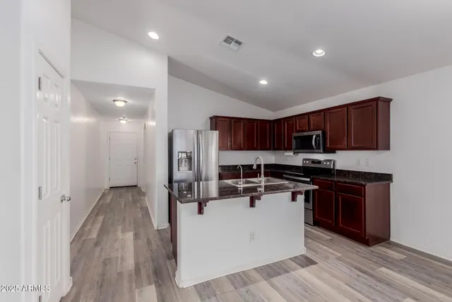 a kitchen with stainless steel appliances a stove top oven a sink a refrigerator white cabinets and wooden floor