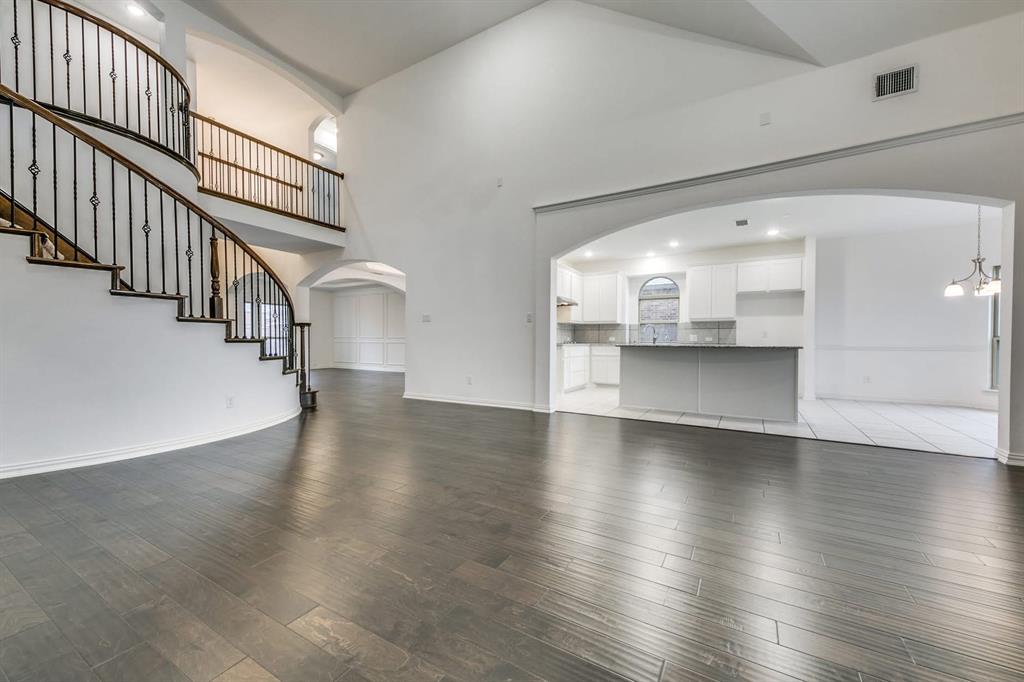 104 Sweetleaf Drive Red Oak, TX 75154 - Photo 13 of 36 The property features striking dark wood flooring throughout the main living area, complemented by a grand curved staircase with ornate iron balusters