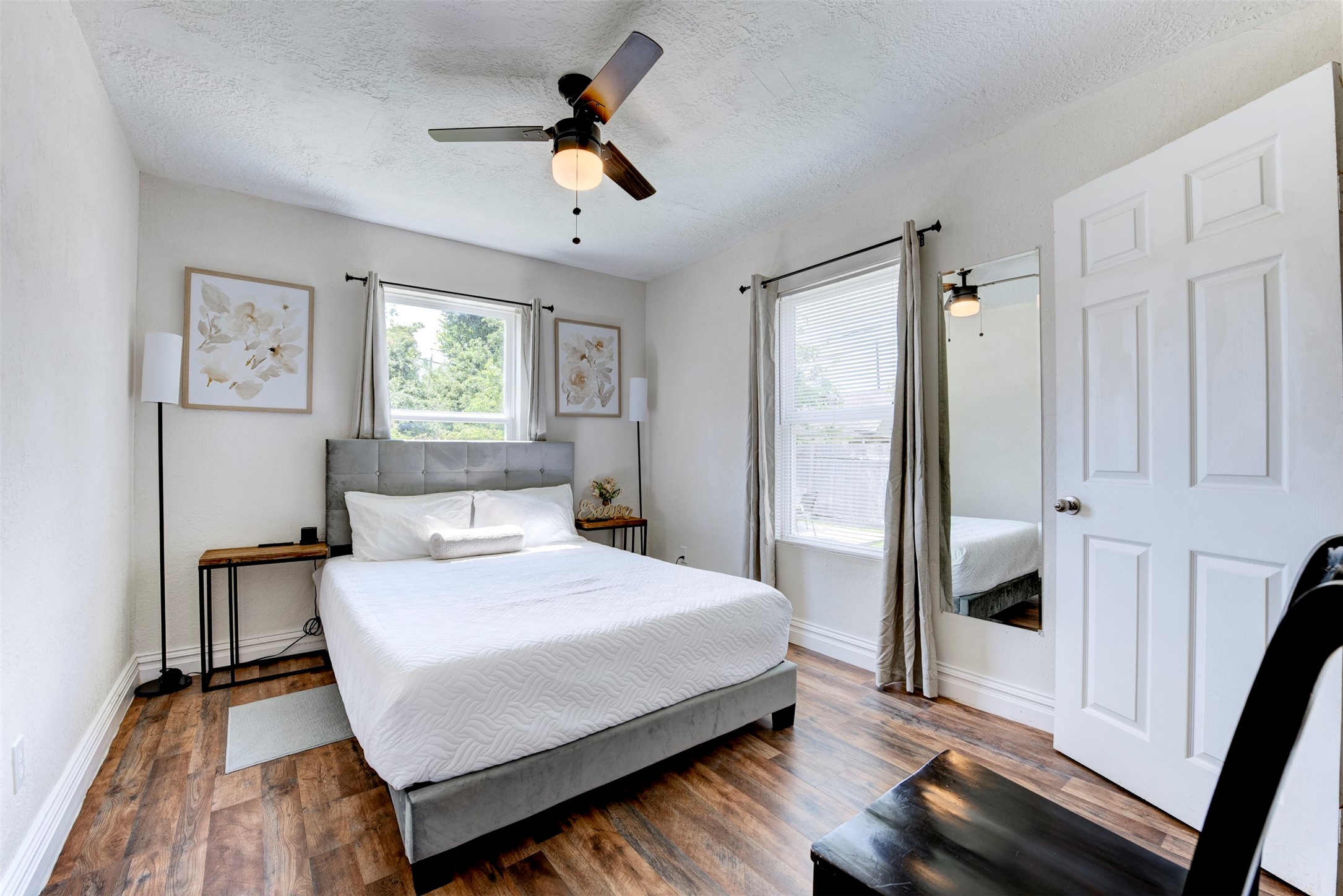 1121 Panama Street Houston, TX 77009 - Photo 17 of 35 Primary bedroom with dark wood-look LVP flooring, ceiling fan with light kit, two windows with grommet curtain panels, full-length mirror, and door leading to private bath.
