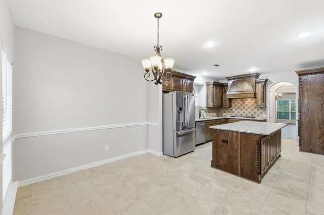 a kitchen with stainless steel appliances granite countertop a refrigerator a sink dishwasher a oven and a dining table with wooden floor